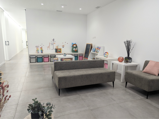 Sala de espera amplia con juegos Sala de espera de Presencia Dental en Massamagrell con sofás y zona infantil con juguetes y pizarra