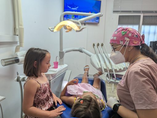 Odontopediatría amable y adaptada Higienista atiende a una niña mientras su hermana observa; consulta infantil con dibujos animados en Presencia Dental